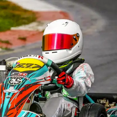 pilota di kart con casco bianco e visiera rossa abbassata. il kart ha dettagli in azzurro e rosso.