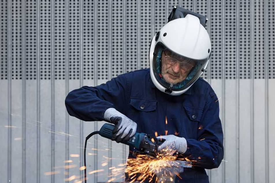 Operaio utilizza una smerigliatrice indossando un casco protettivo per proteggersi dalle scintille